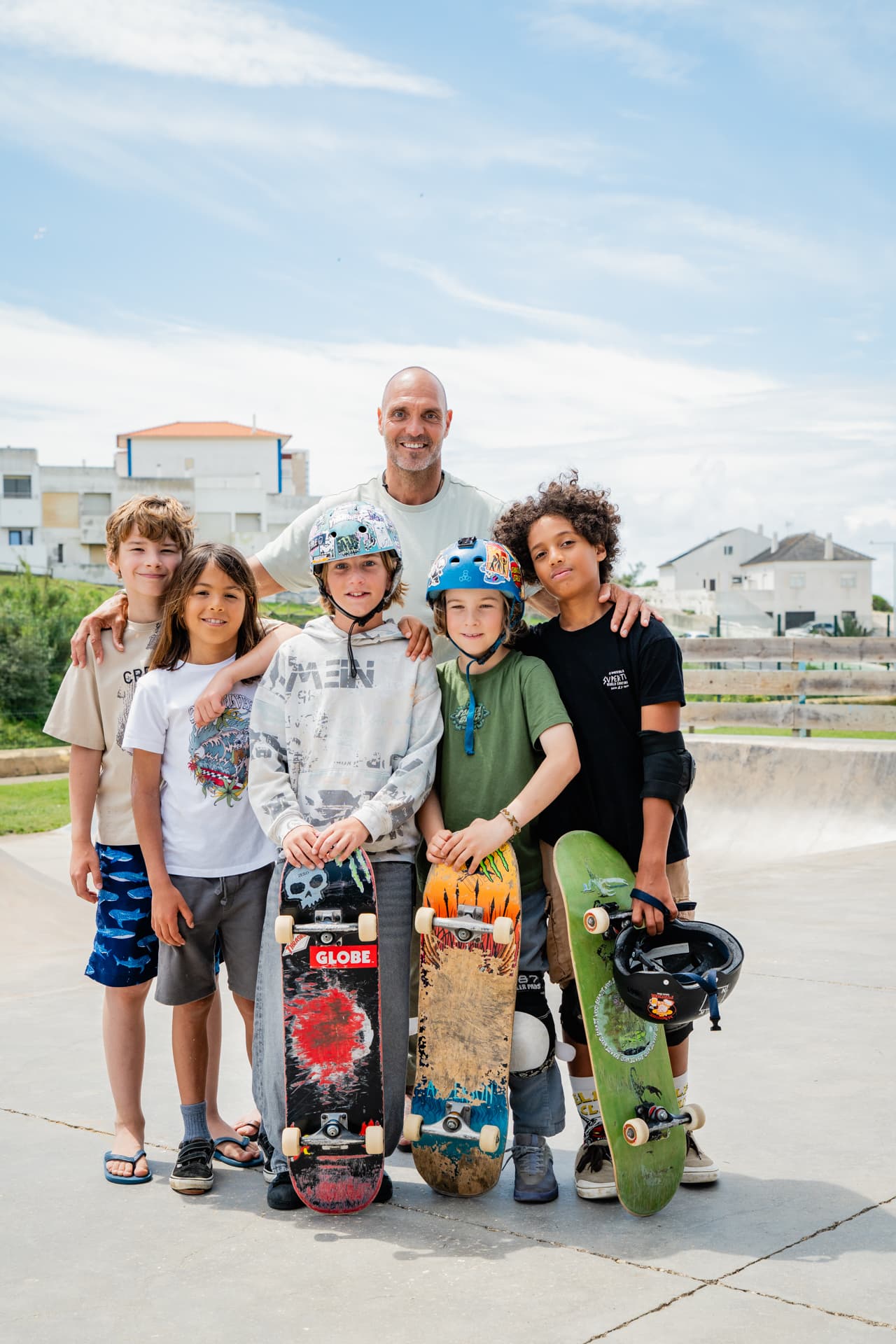 A coach standing with five boys holding their skateboards at the skatepark